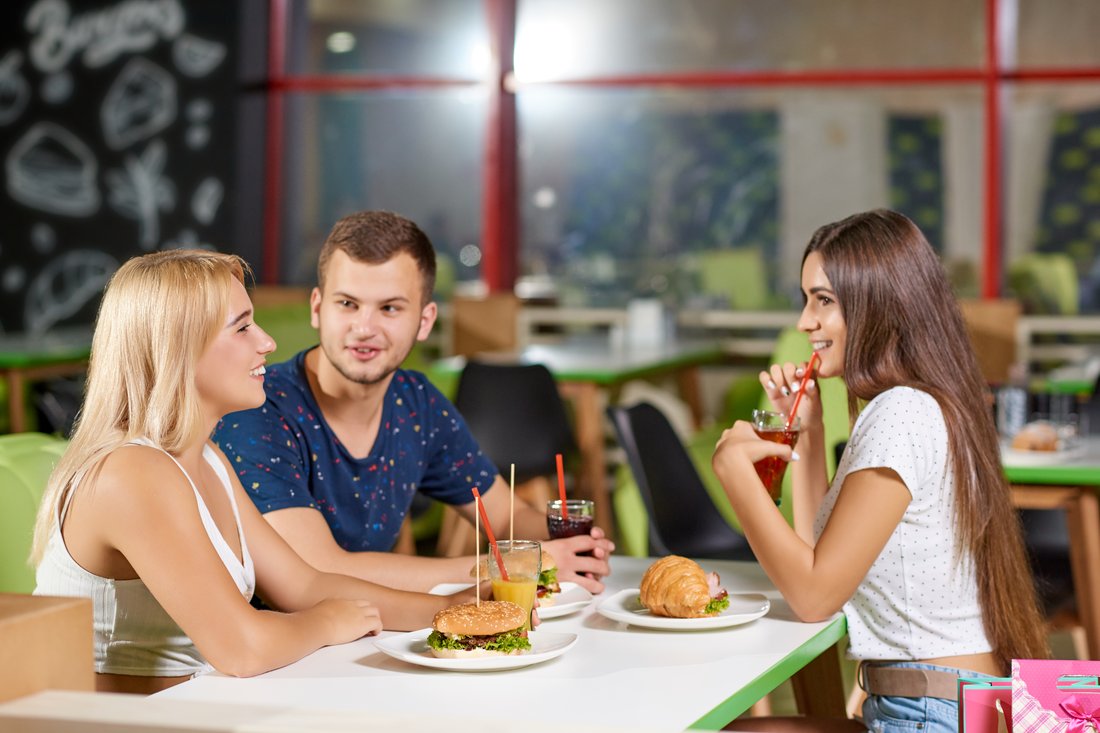 Troje znajomych je burgery i rozmawia przy stoliku w kawiarni