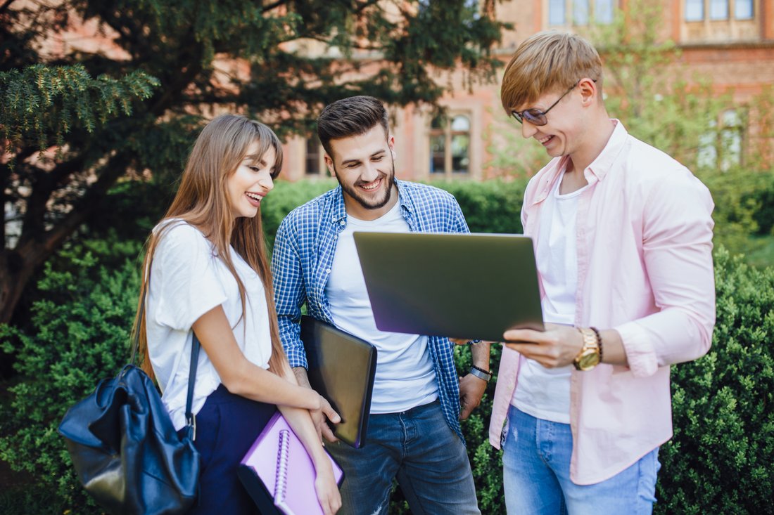 Troje studentów ogląda coś na laptopie i śmieje się na kampusie